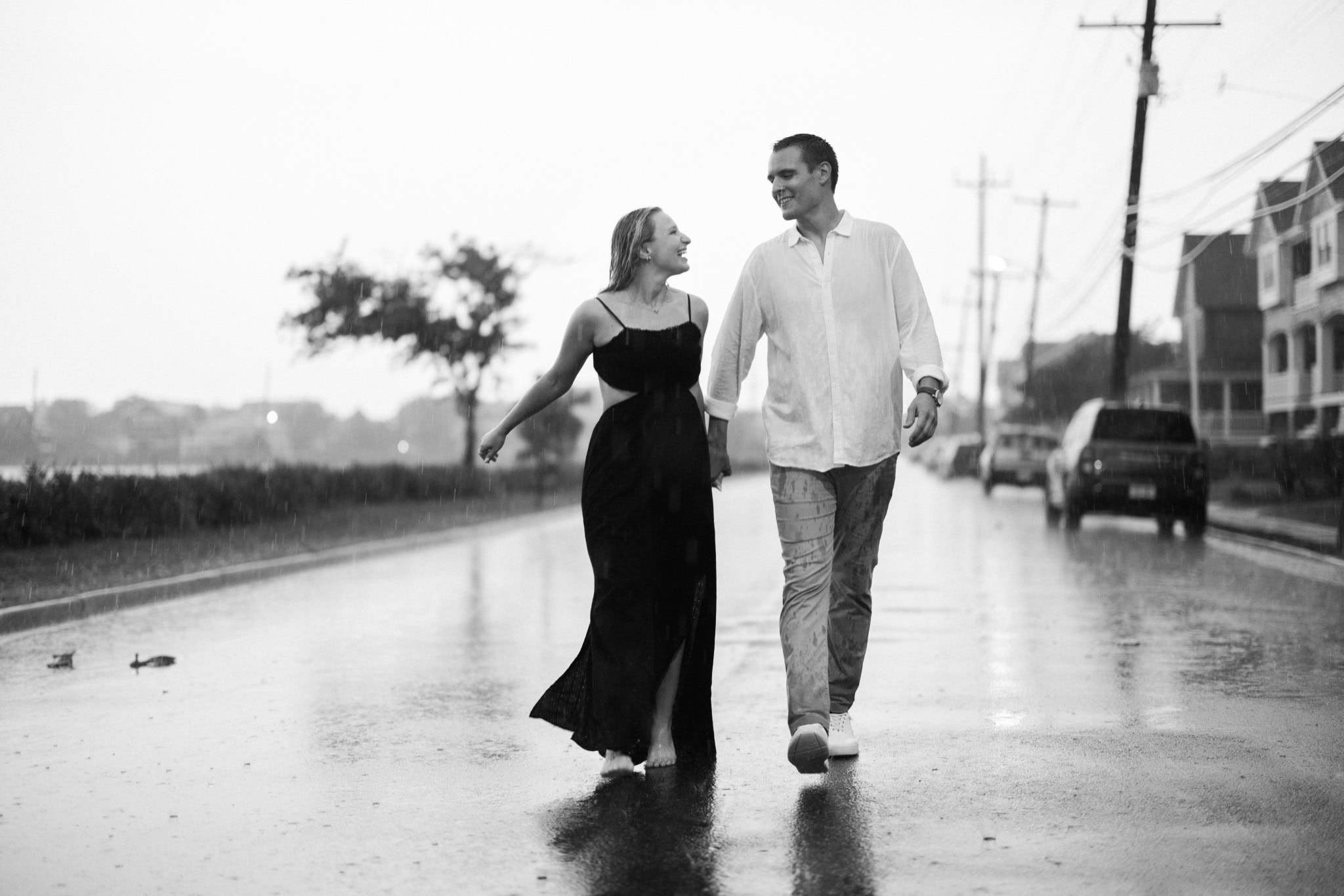 Black and white image of a newly engaged couple walking down a rainy Bay Head NJ street