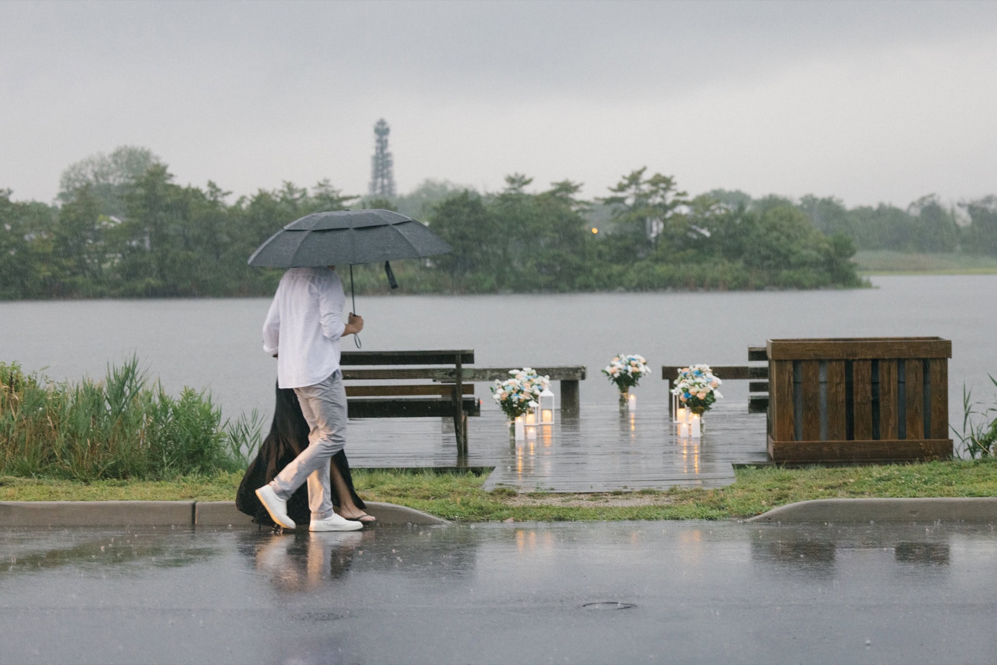 Groom walking up under an umbrella to a candlelit dock on Twilight Lake for a rainy surprise proposal in Bay Head NJ