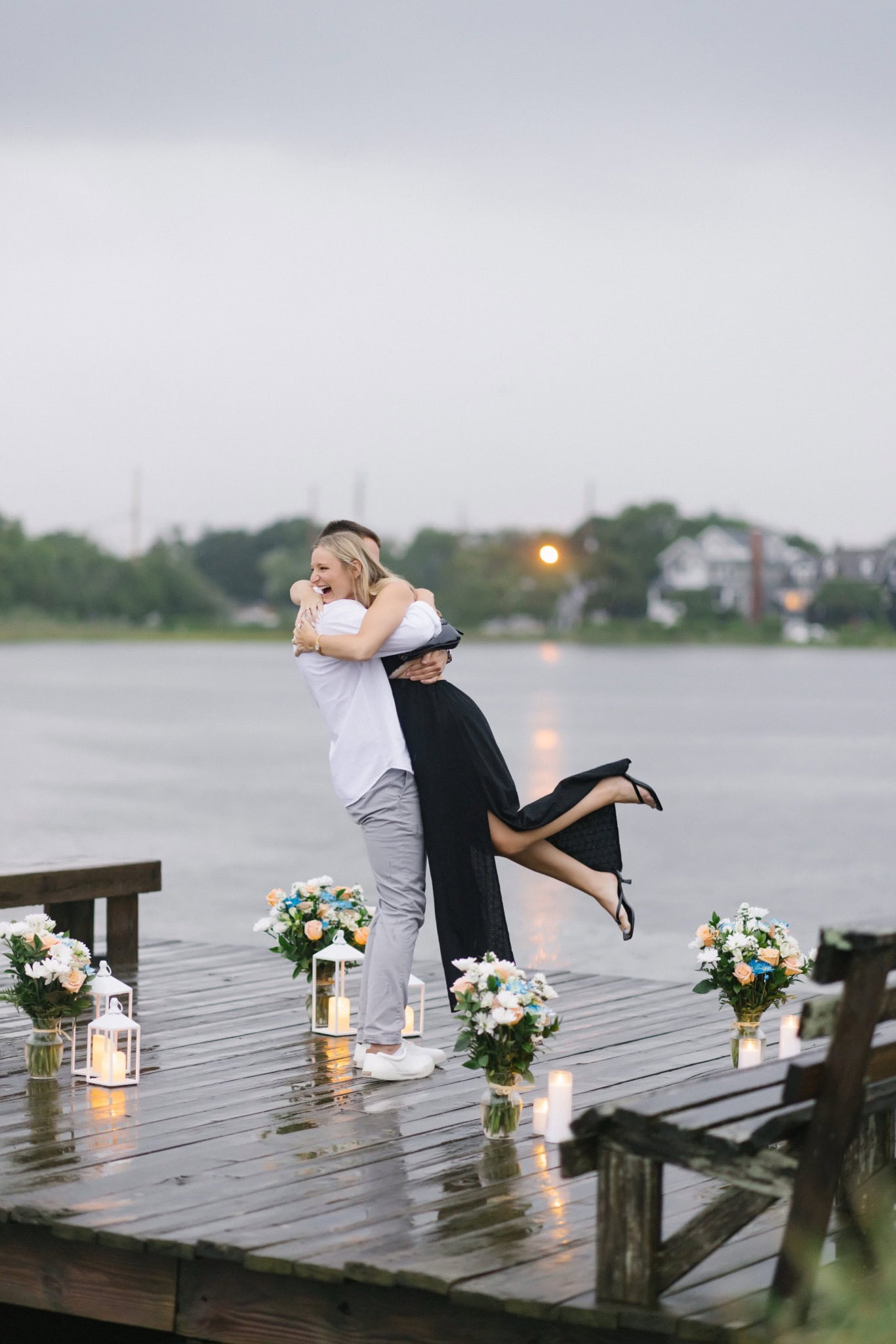 Newly engaged couple laughing as he lifts her on a candlelit dock in Bay Head NJ