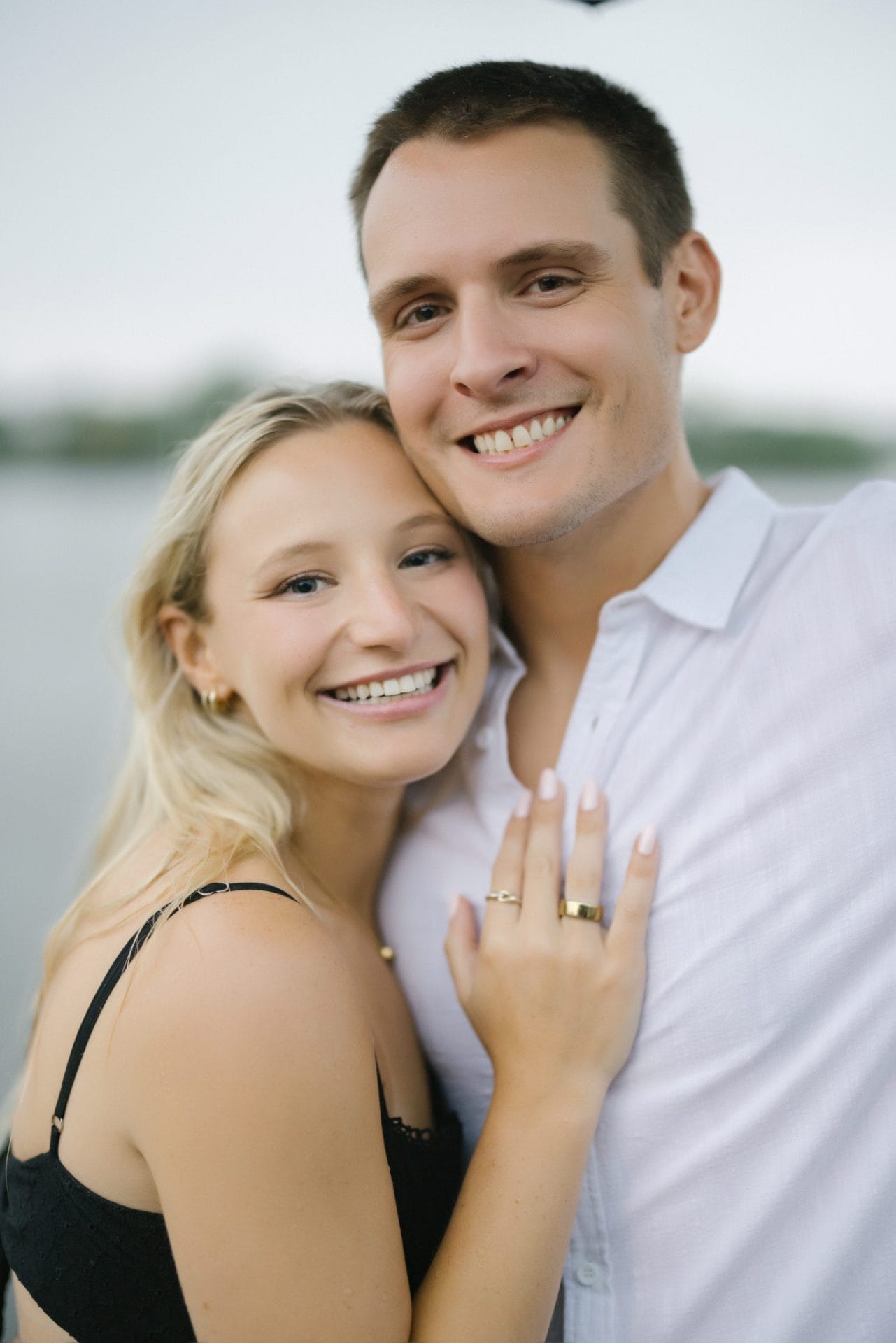 Newly engaged couple smiling cheek to cheek as she shows her engagement ring after a surprise proposal in Bay Head NJ