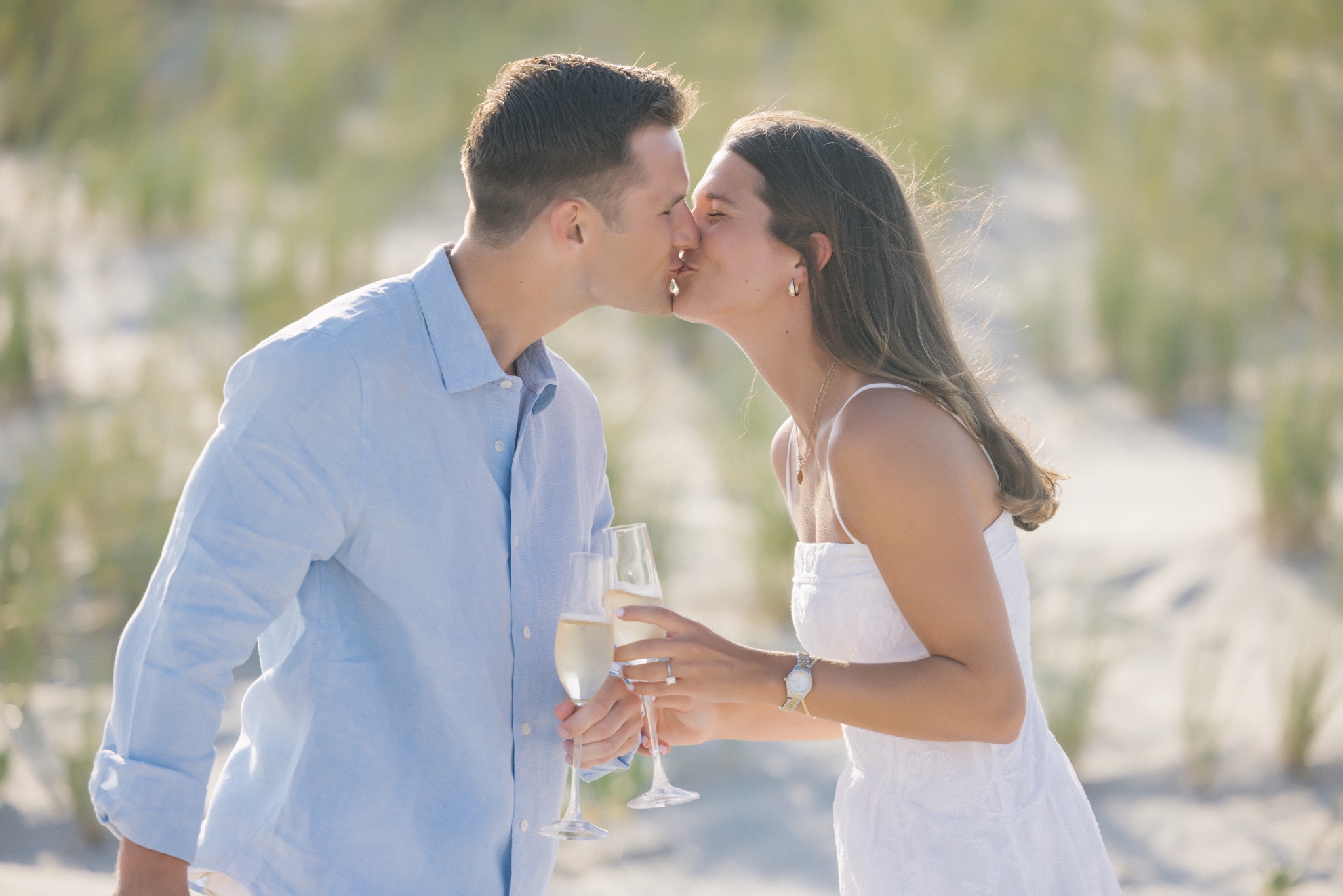 Katie and Chris kissing while holding champagne glasses on the beach in Stone Harbor, New Jersey