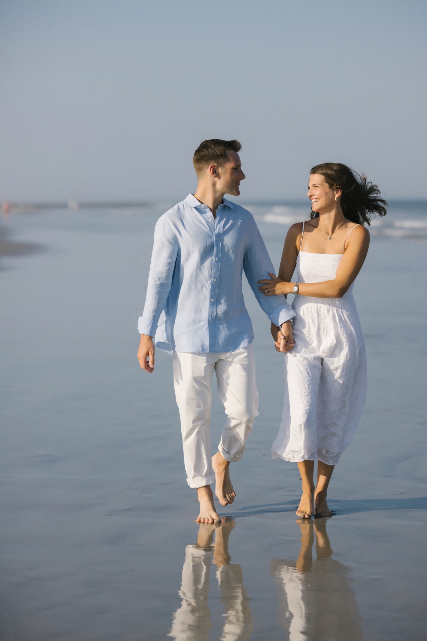 Katie and Chris holding hands and walking barefoot along the water's edge in Stone Harbor, New Jersey
