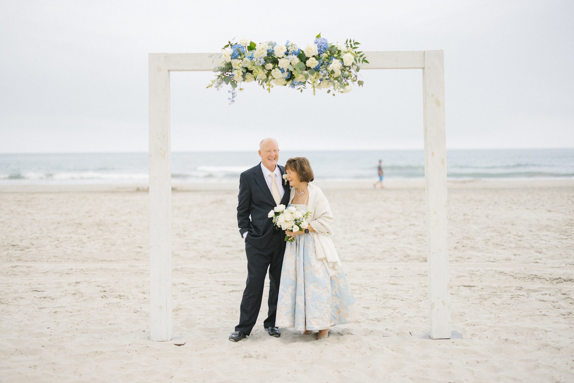 A couple under a floral arch during their beach vow renewal ceremony in Avalon, New Jersey