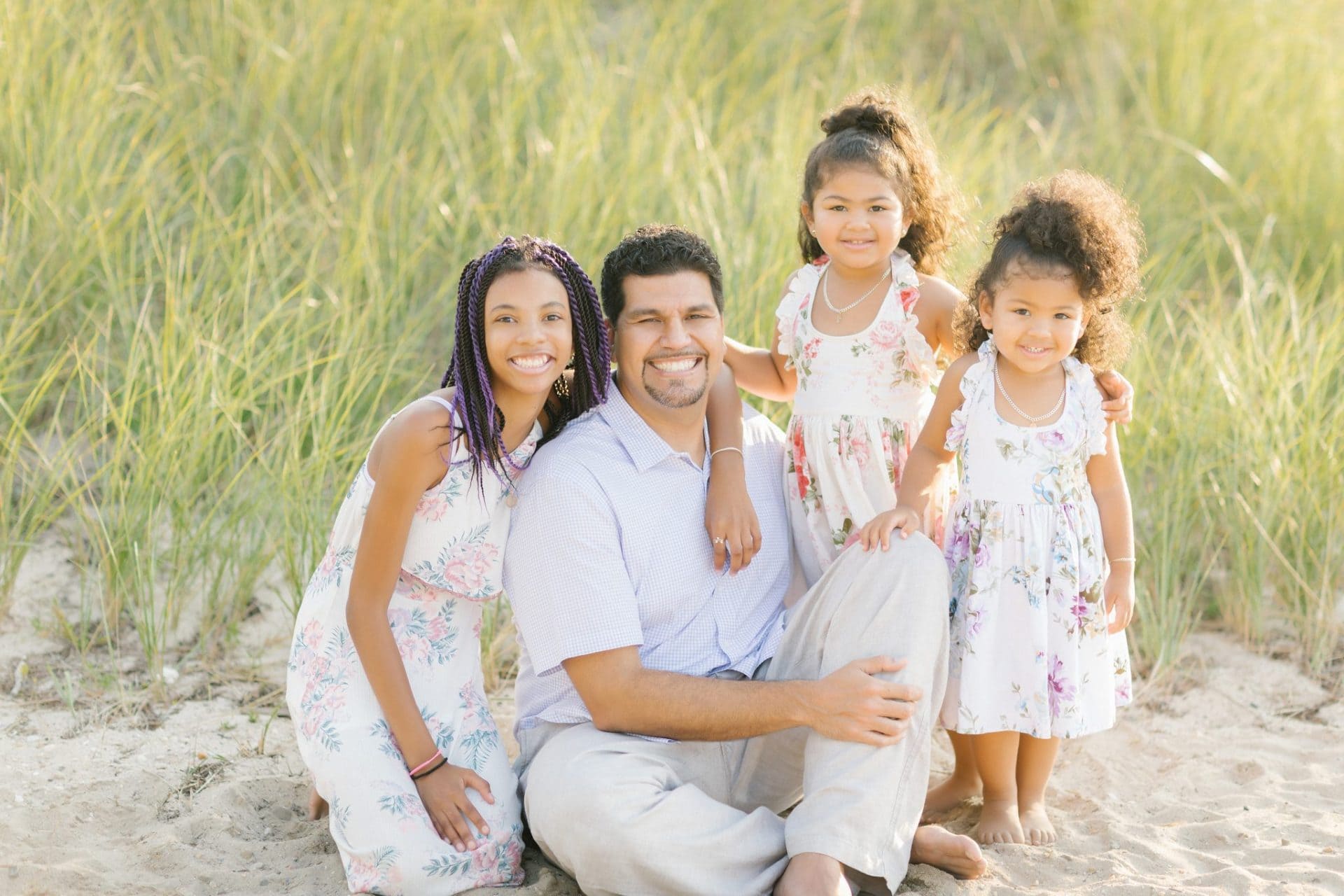 A father sitting with his three daughters gathered around him in the dune grass during a Beach Haven family session