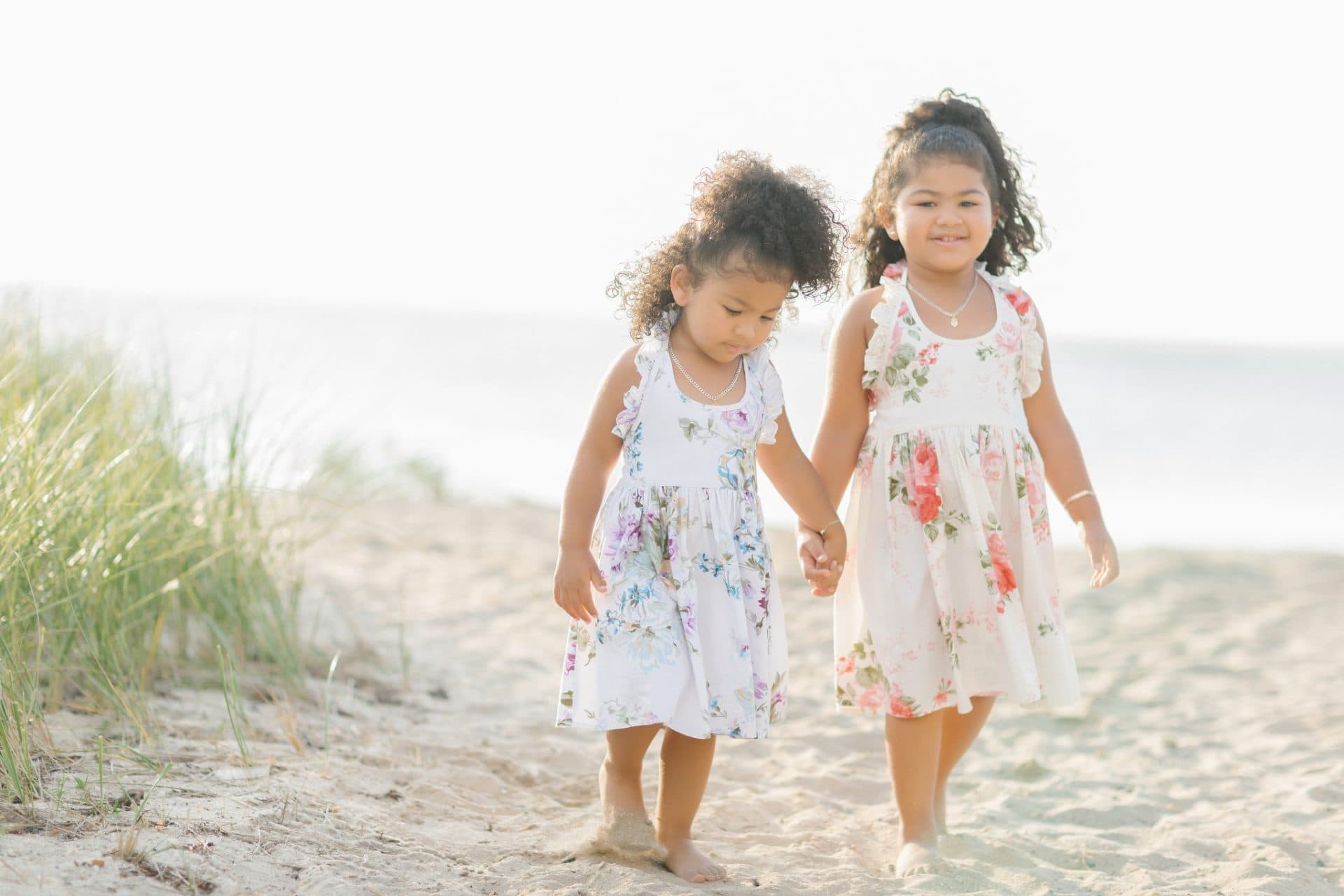 Two sisters walking hand in hand across the sand with the bay behind them in Beach Haven, New Jersey