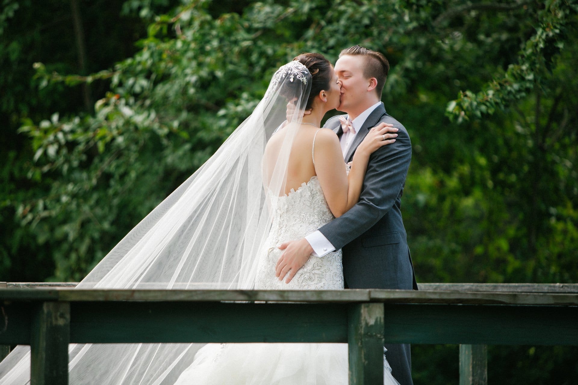 Bride and groom kissing on the bridge at Berlin Park, veil trailing behind