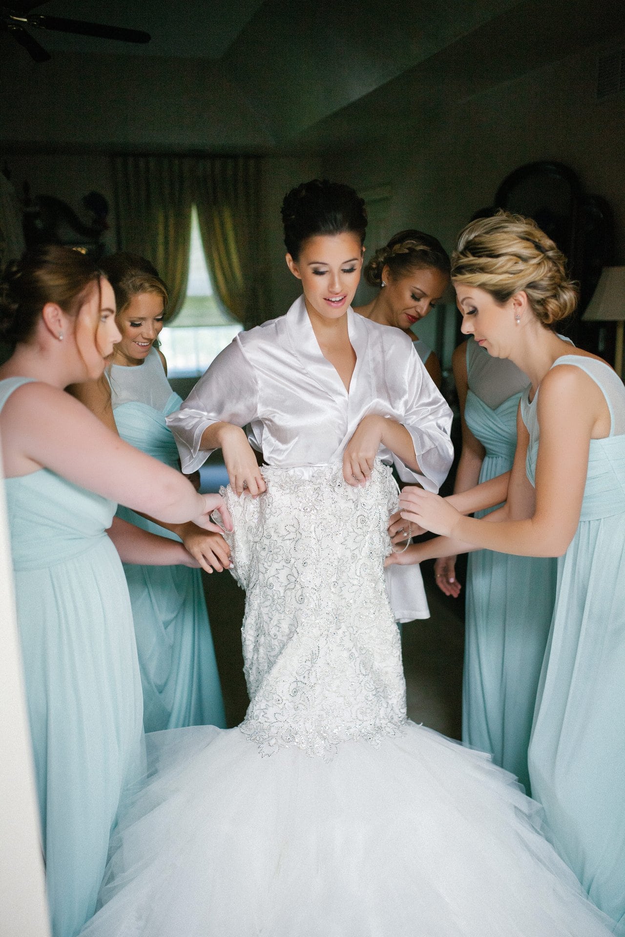 Bridesmaids in mint helping the bride into her gown at her parents' house