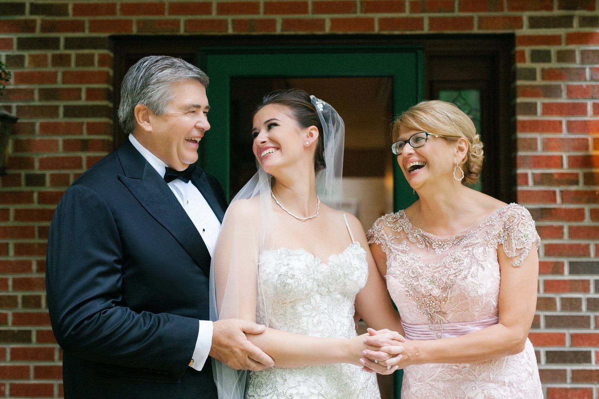 Bride laughing with both parents outside the house she grew up in