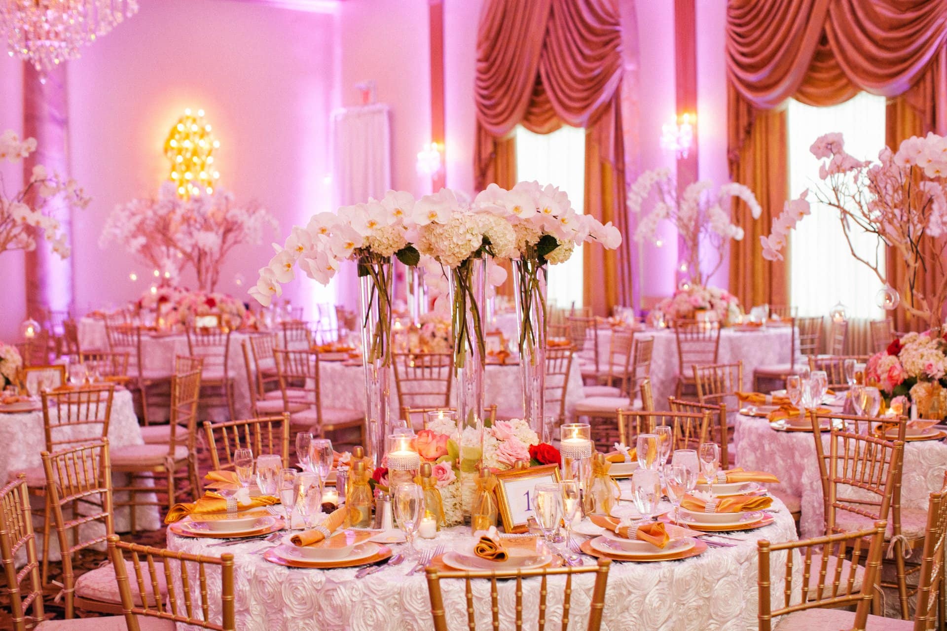 Tall white centerpieces and gold chairs set for more than 200 guests