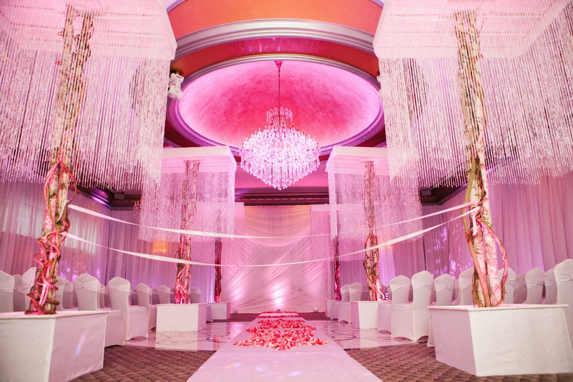 Ceremony room at Lucien's Manor with crystal strand canopies over white pedestals and a rose petal aisle