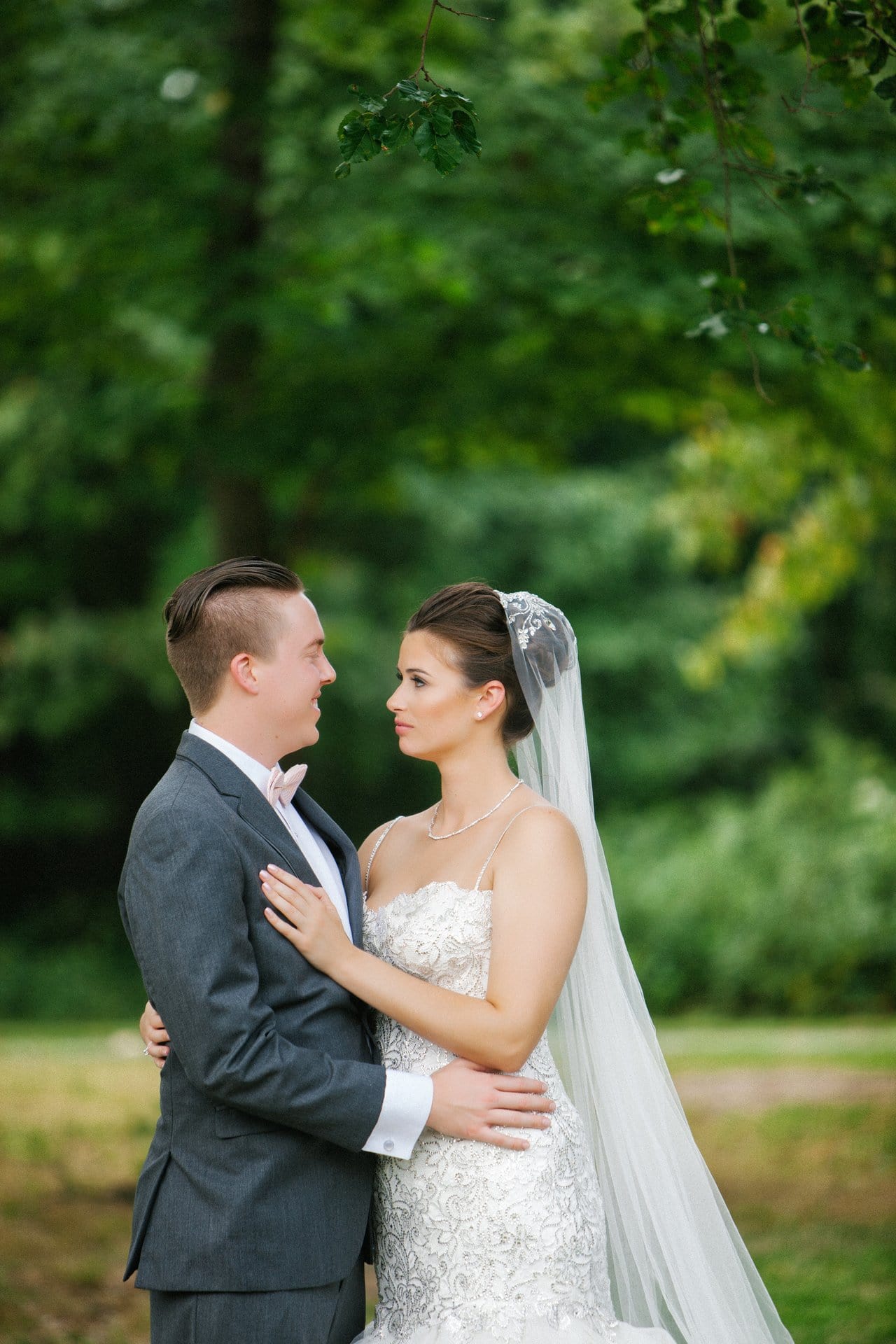 Bride and groom looking at each other, wooded park behind them