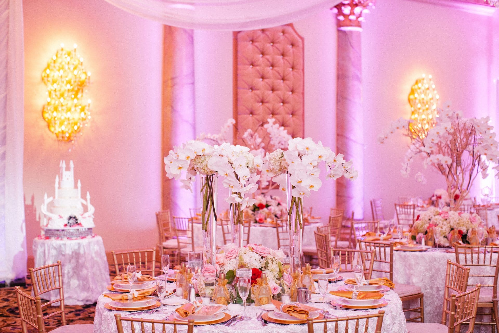 Reception tables set in gold and blush under pink uplighting at Lucien's Manor