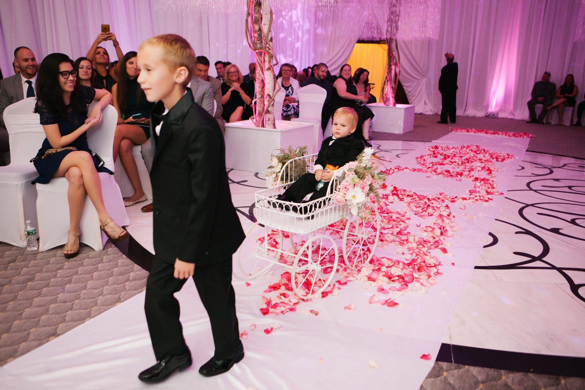 Ring bearer pulling a flower cart down the petal-covered aisle