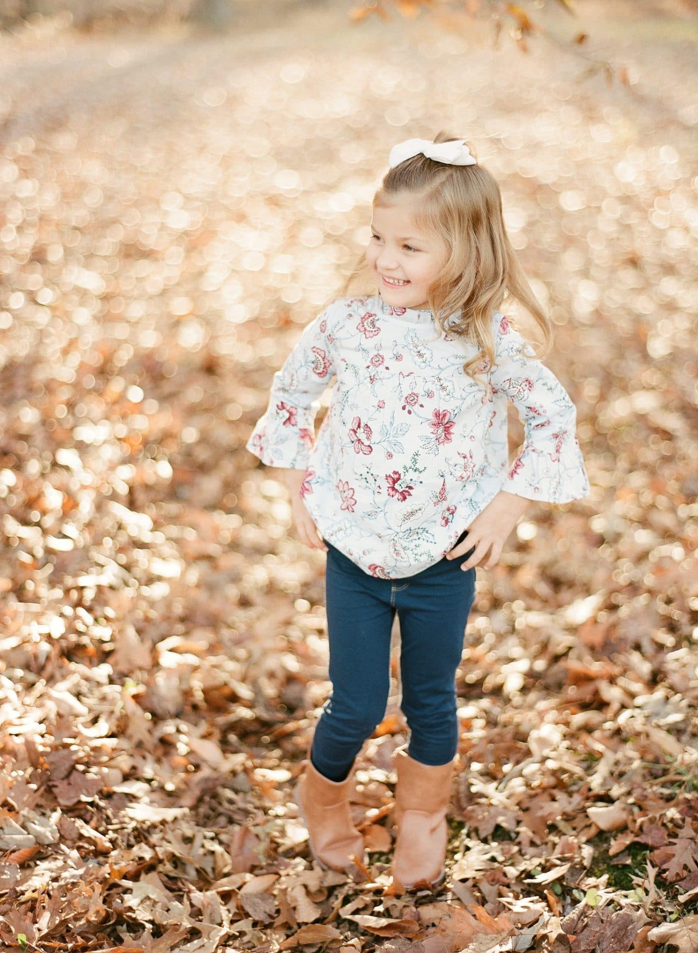A young girl with her hands on her hips looking off to the side in the fall leaves in Medford, New Jersey