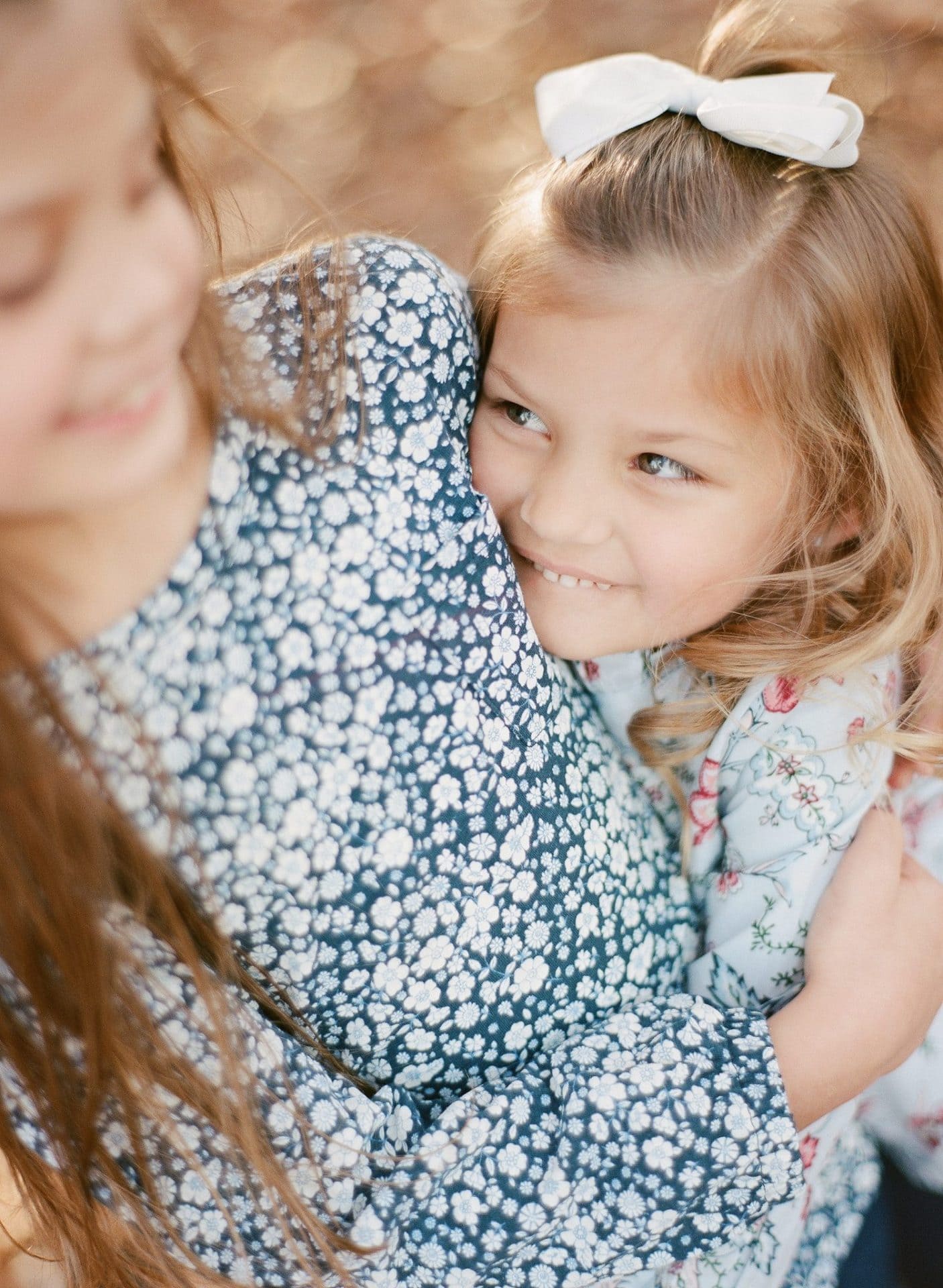 A young girl resting her head on her big sister's shoulder and looking at the camera during a fall session in Medford, New Jersey