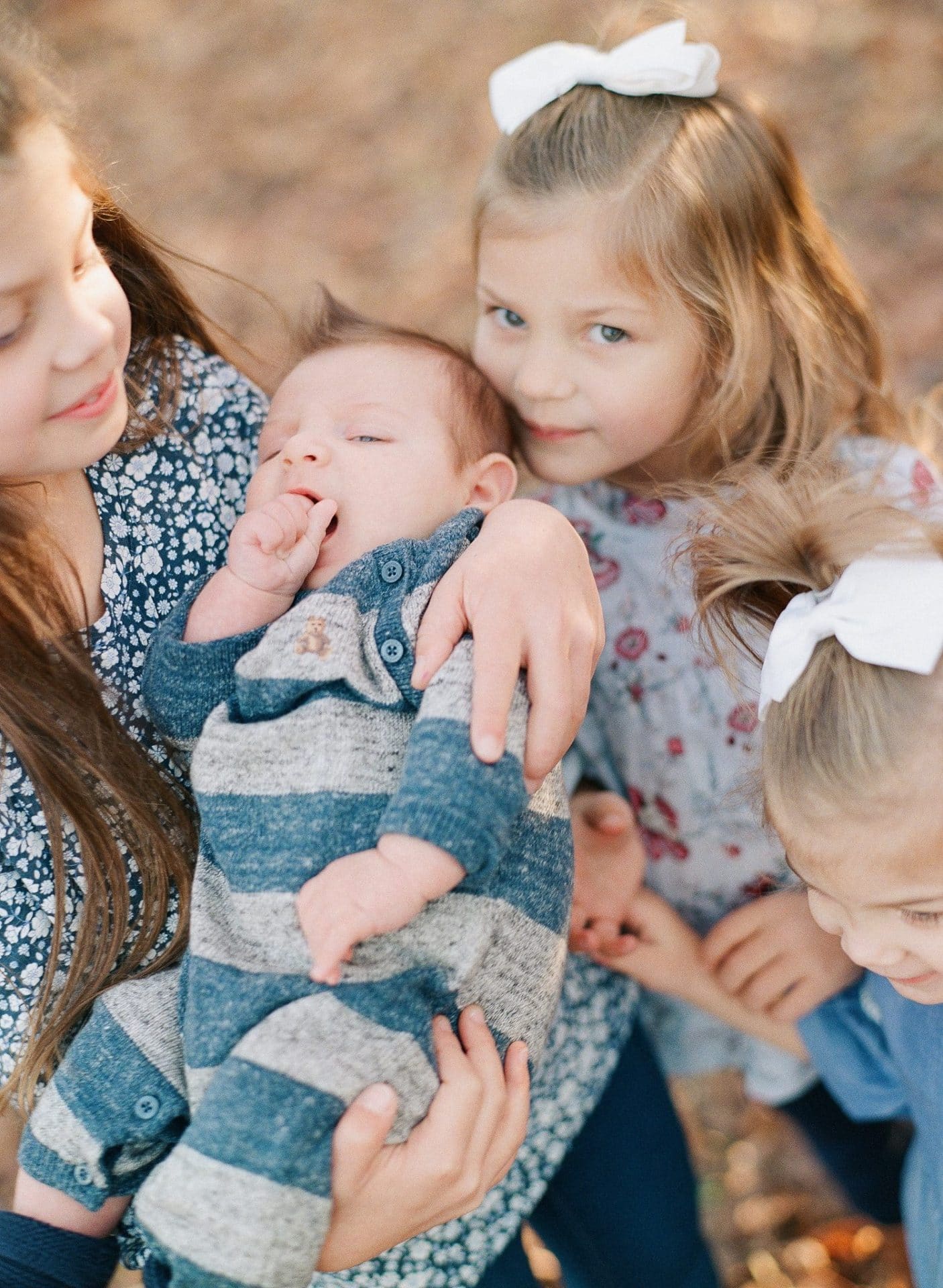 Three sisters gathered in around the baby, the oldest holding the baby while the others lean their heads in, in Medford, New Jersey