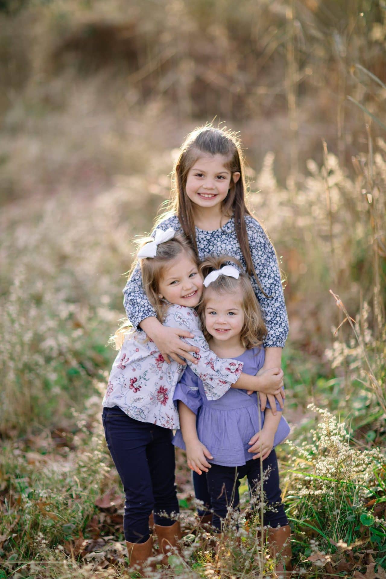 Three sisters standing together in tall seed grass at the end of a fall session in Medford, New Jersey