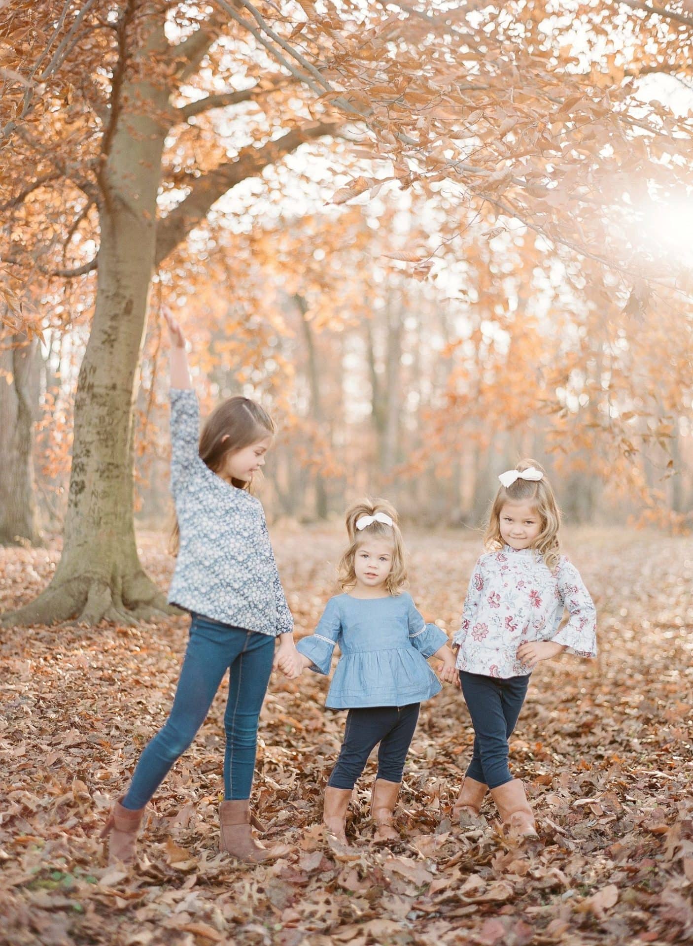 Three sisters under a big beech tree, the youngest holding both her sisters by the hand, during a fall session in Medford, New Jersey