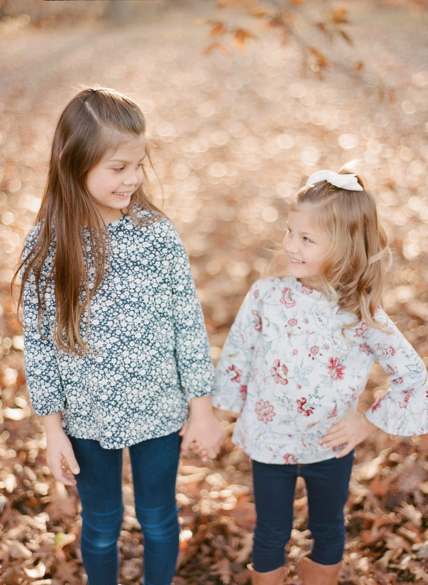 Two older sisters holding hands and looking at each other in the autumn woods in Medford, New Jersey