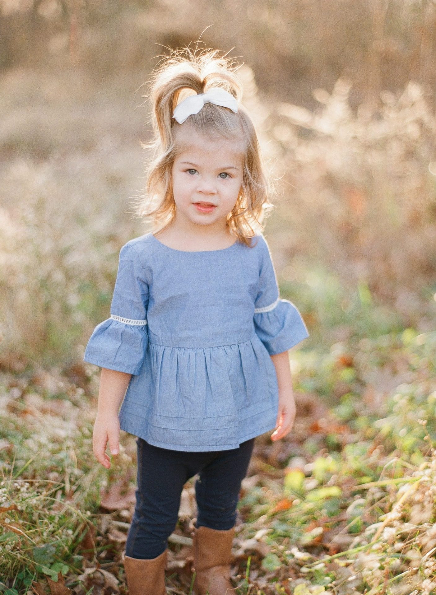 The youngest sister standing in a backlit meadow of tall seed grass with her hair lit from behind in Medford, New Jersey