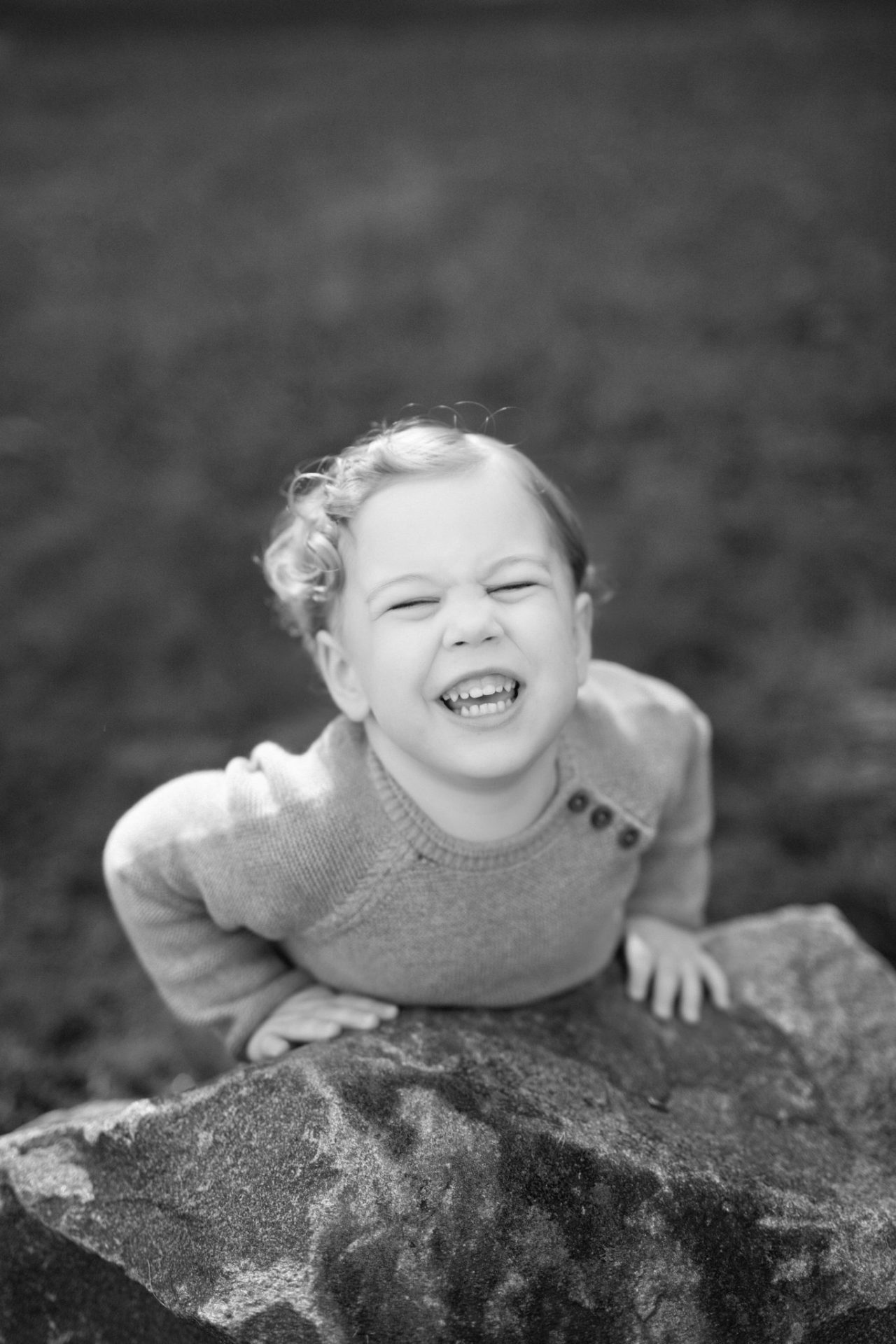 A black and white photograph of a laughing boy climbing up onto a rock at Laurel Acres Park in Mount Laurel, New Jersey