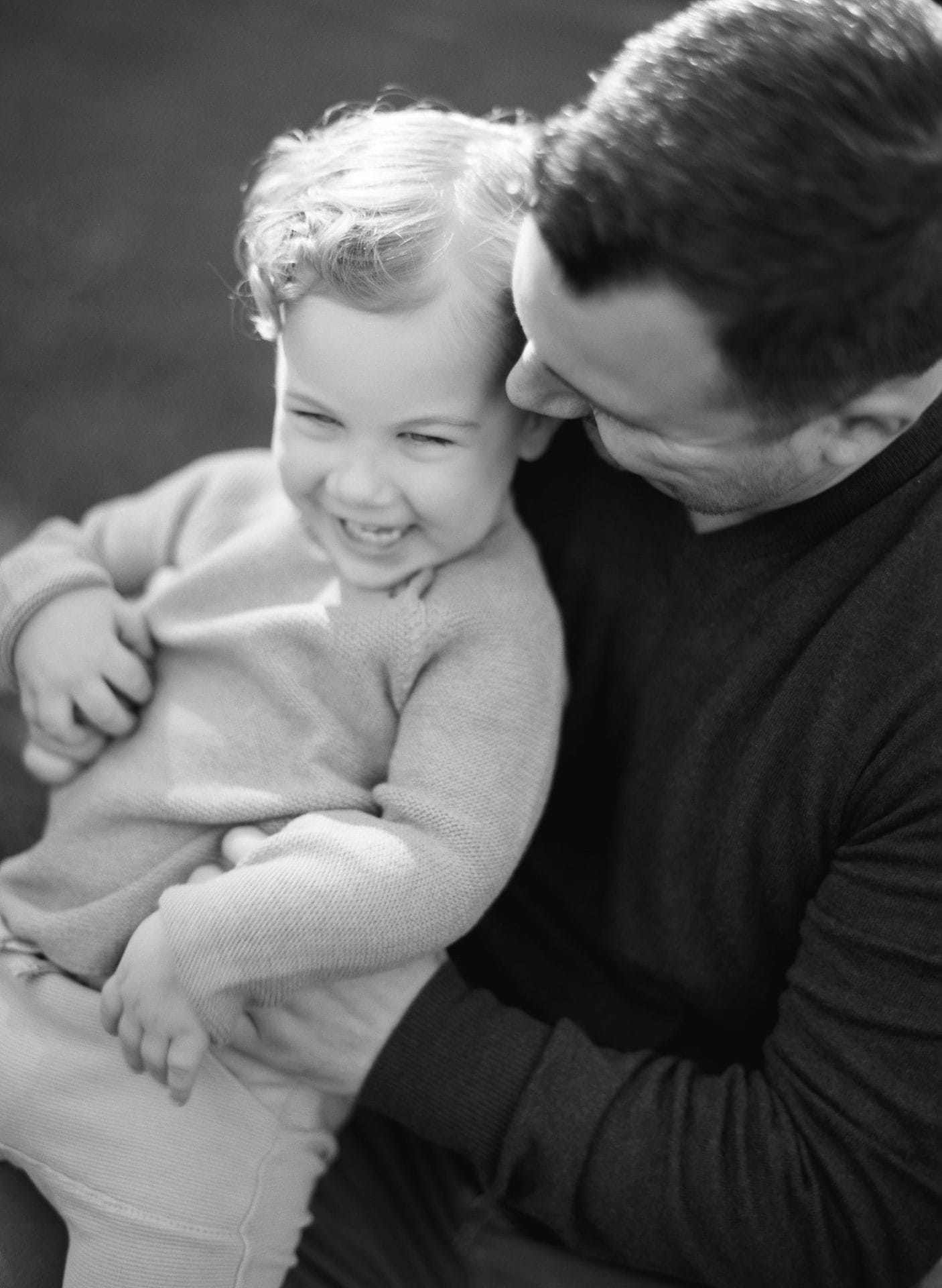 A black and white photograph of a dad wrapping his arms around his son during a family session in Mount Laurel, New Jersey
