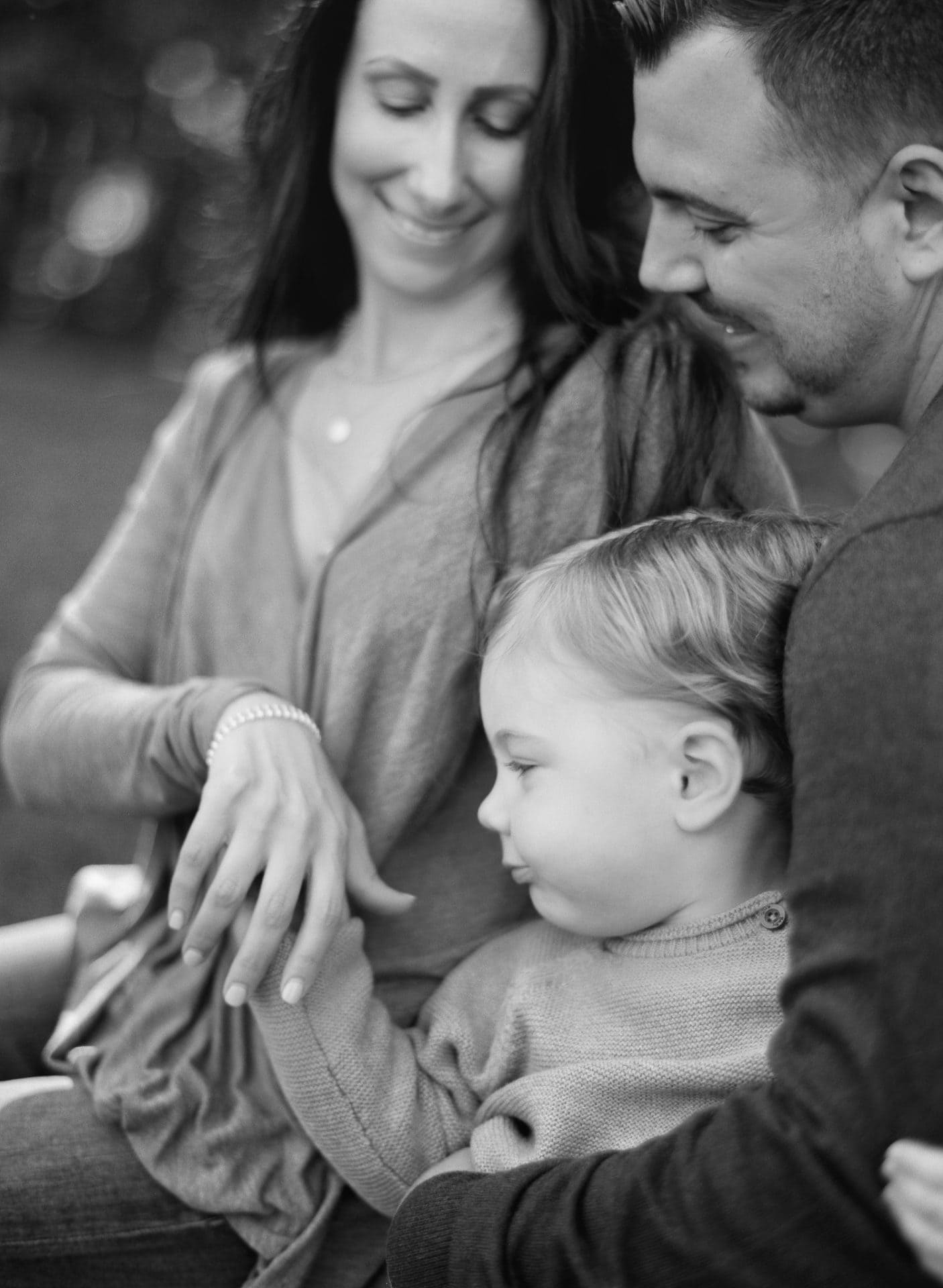 A black and white photograph of a mom and dad looking down at their son during a family session in Mount Laurel, New Jersey