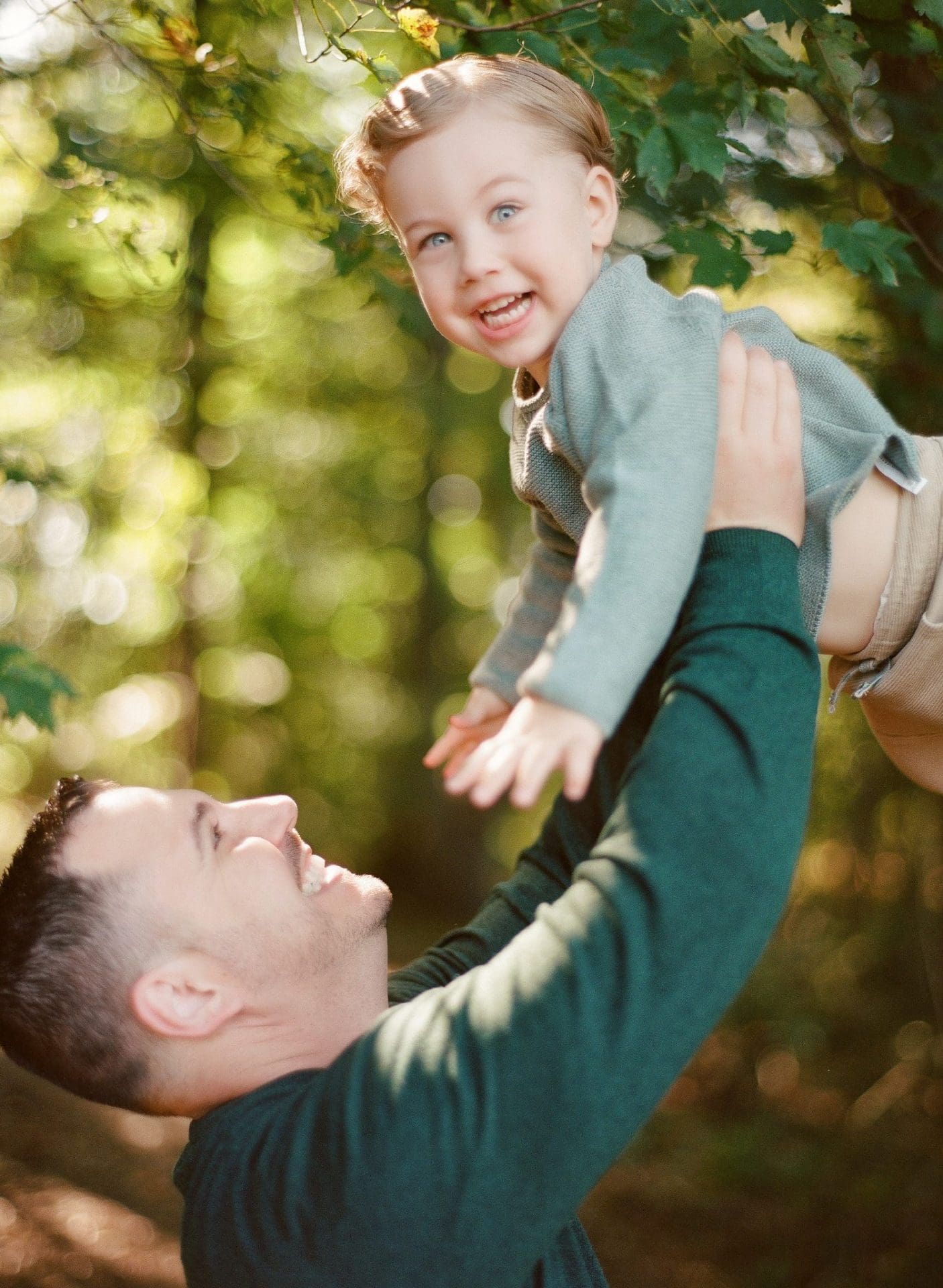 A dad lifting his son up into the air under a green canopy at Laurel Acres Park in Mount Laurel, New Jersey