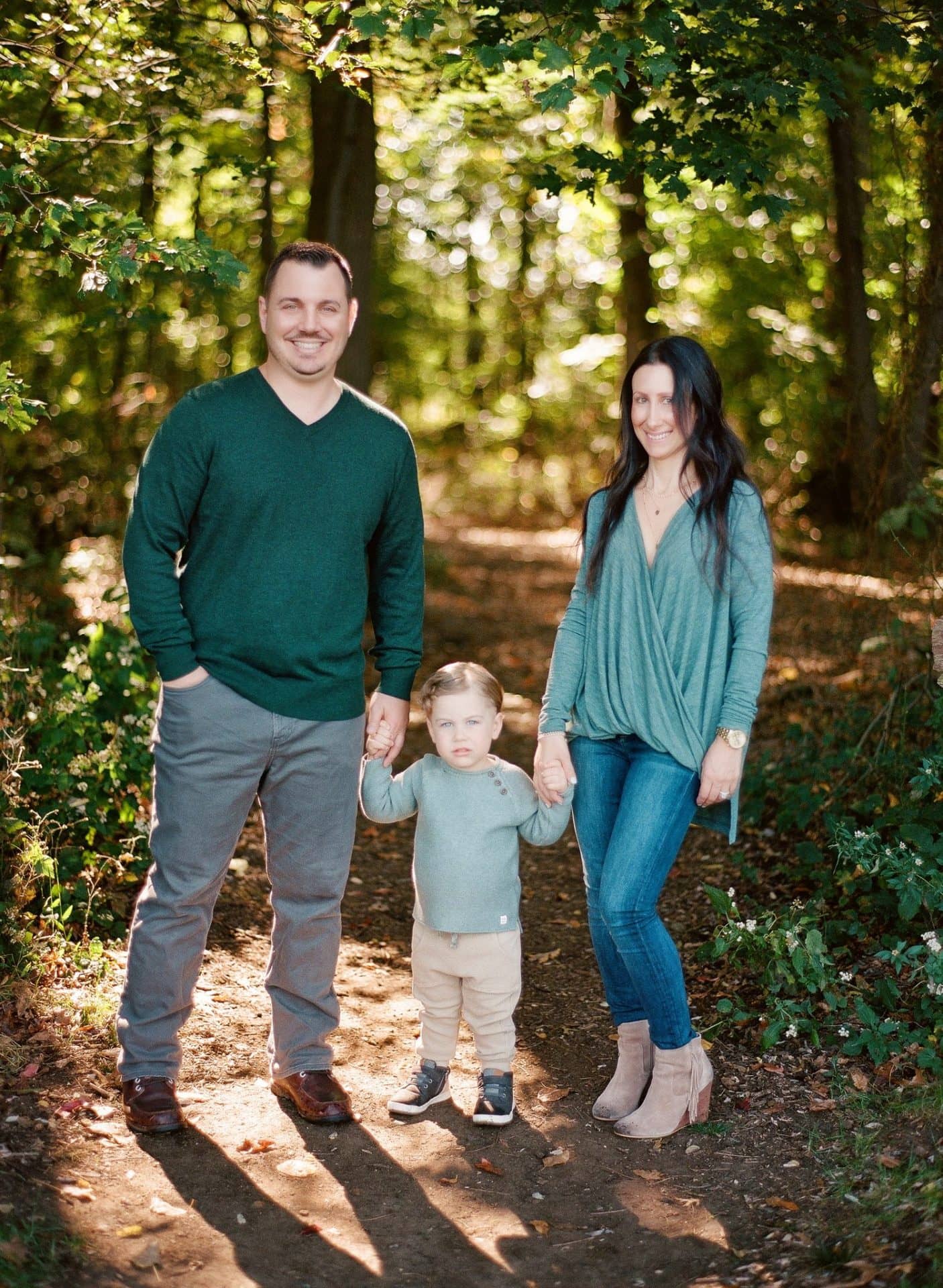 A family of three standing together on a shaded path in the woods at Laurel Acres Park in Mount Laurel, New Jersey