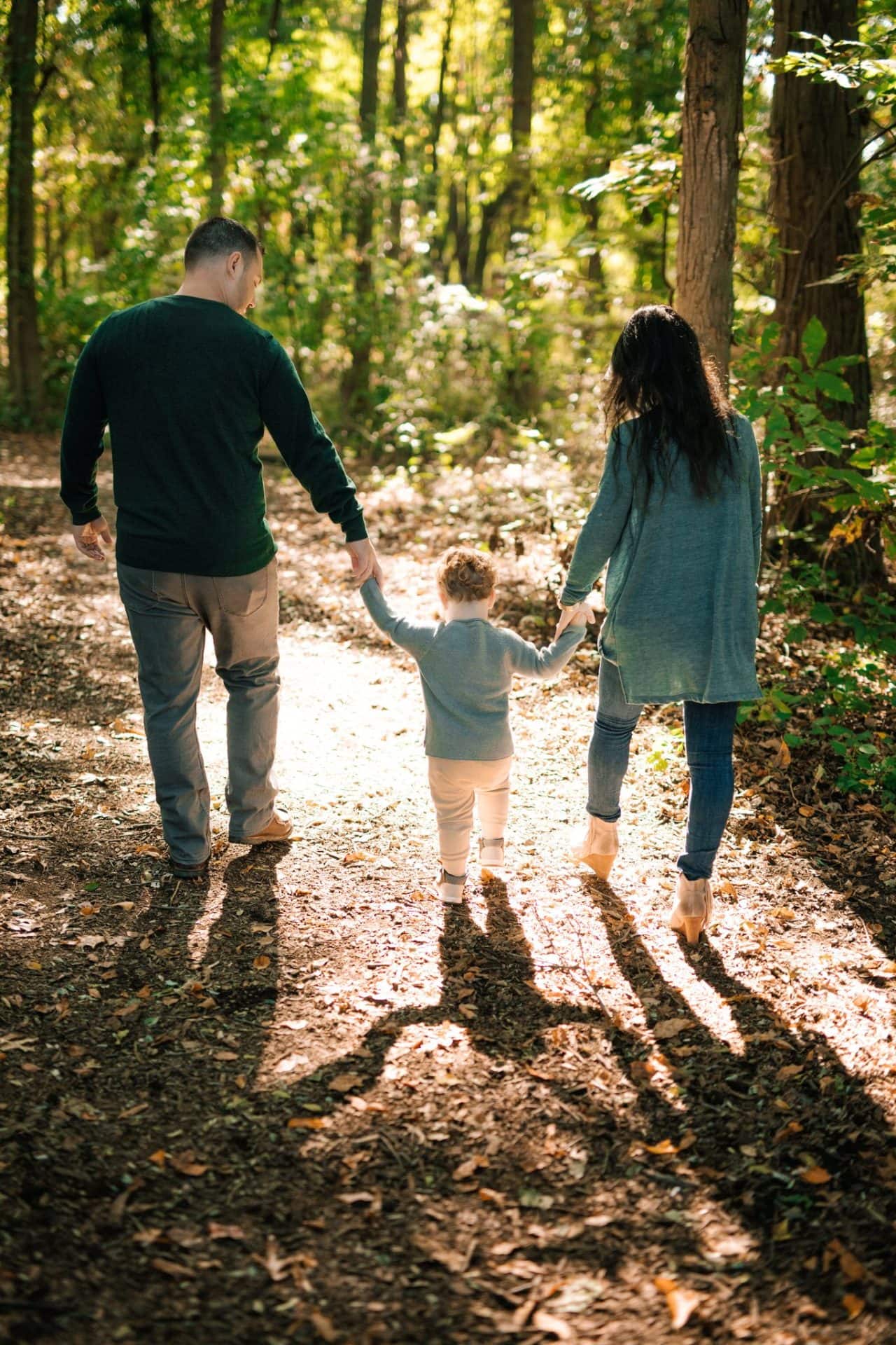 A family of three walking away hand in hand down a leaf covered path at Laurel Acres Park in Mount Laurel, New Jersey