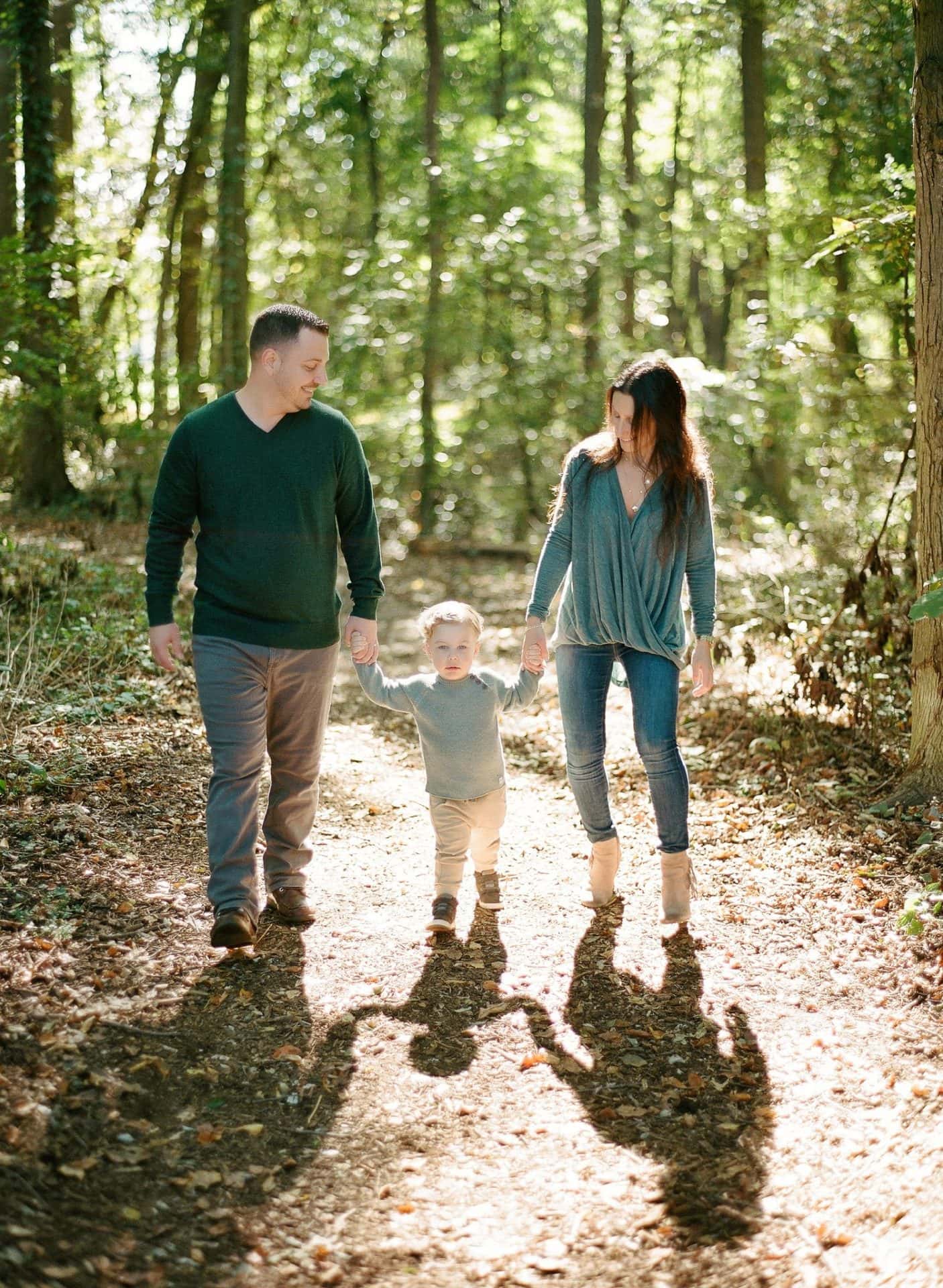 A mom and dad walking their son down a wooded path with the late morning sun behind them in Mount Laurel, New Jersey