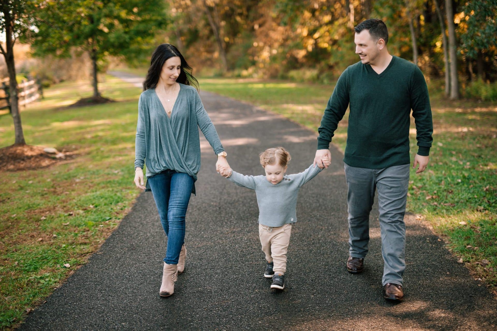 A mom and dad walking their son down the paved path with autumn trees behind them at Laurel Acres Park in Mount Laurel, New Jersey