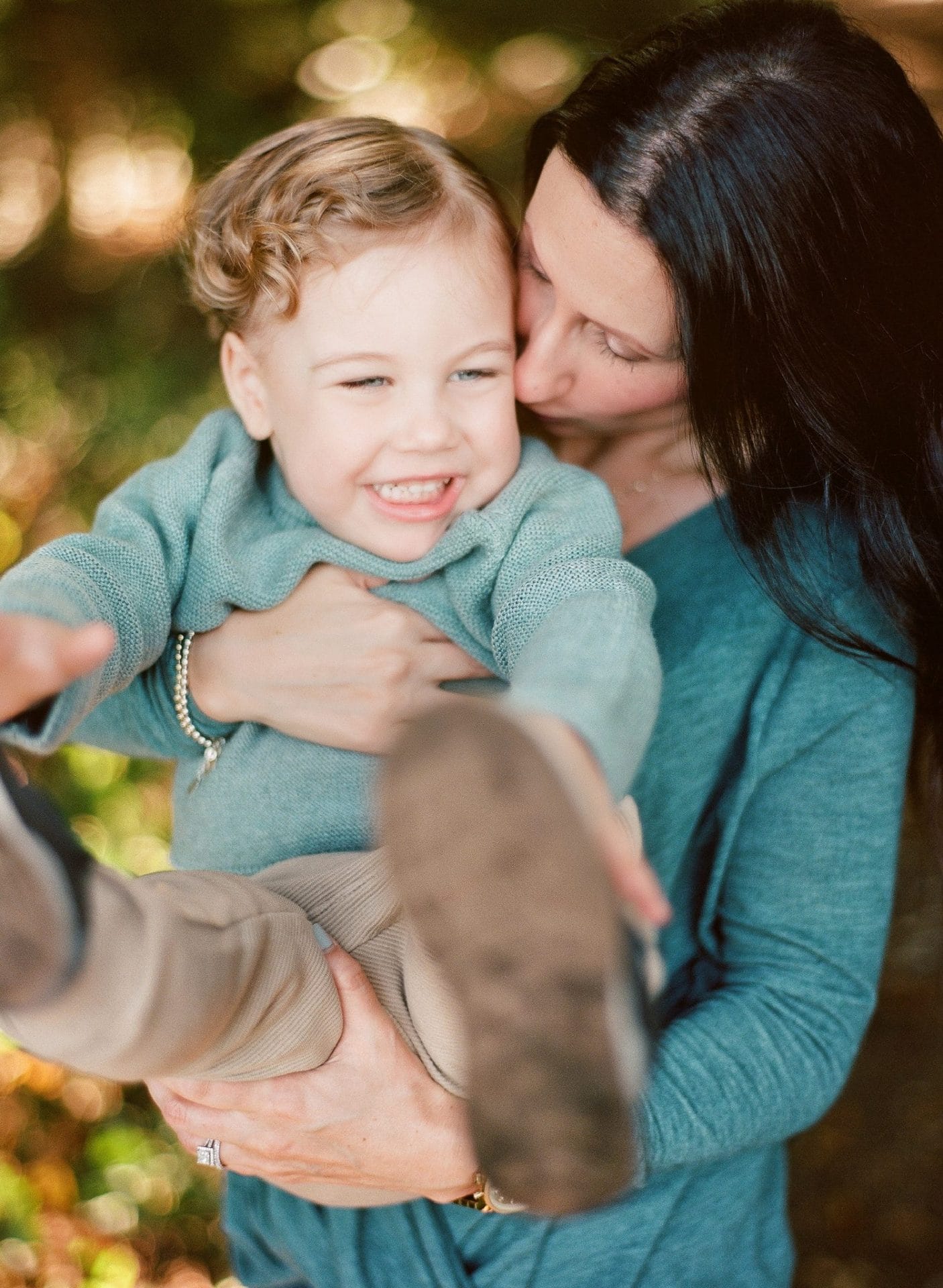 A mom holding her son as he laughs and kicks during a family session in the woods in Mount Laurel, New Jersey