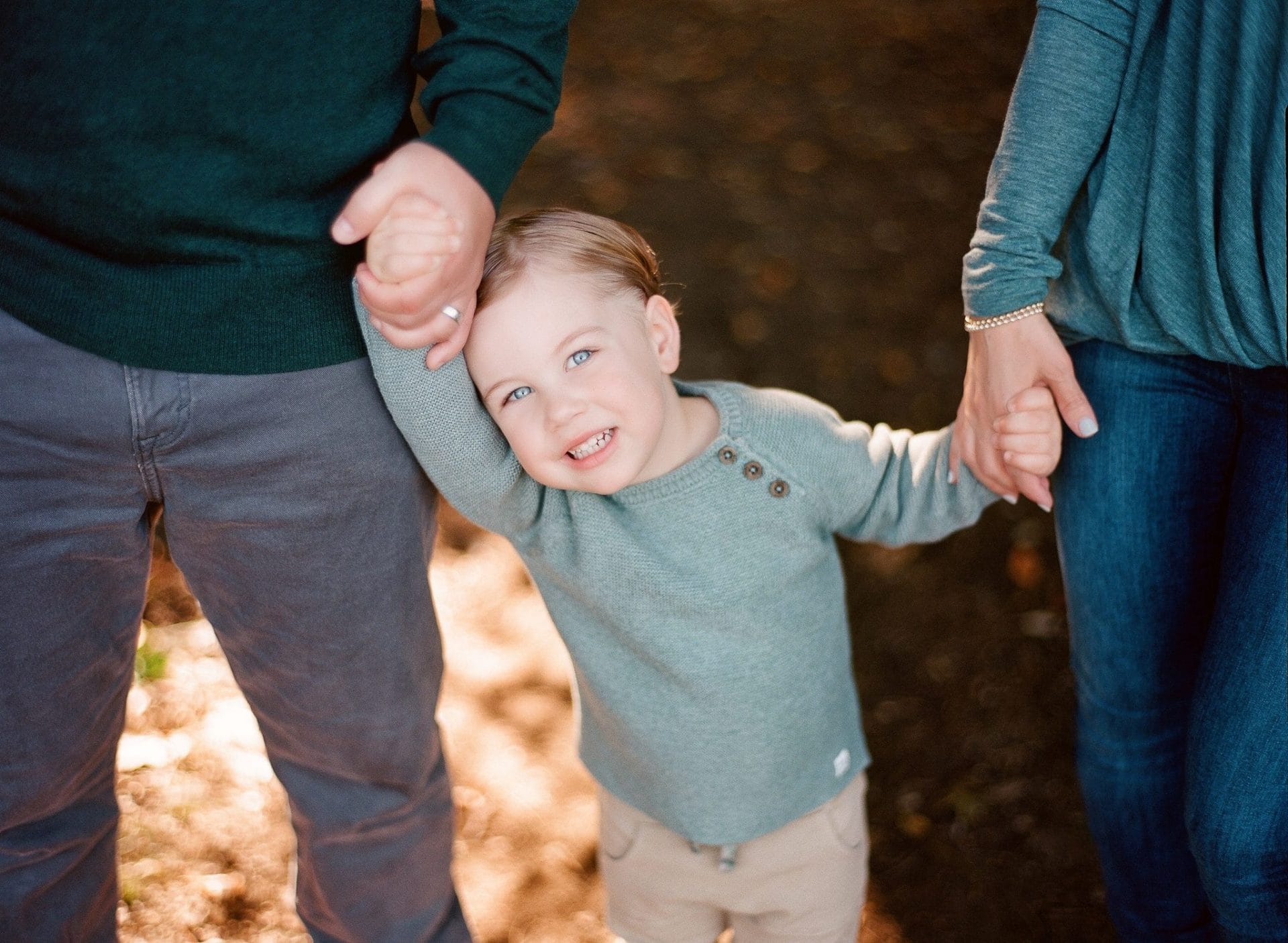 A small boy standing between his parents with a hand held on each side, his head tipped against his dad's arm, during a family session in Mount Laurel, New Jersey