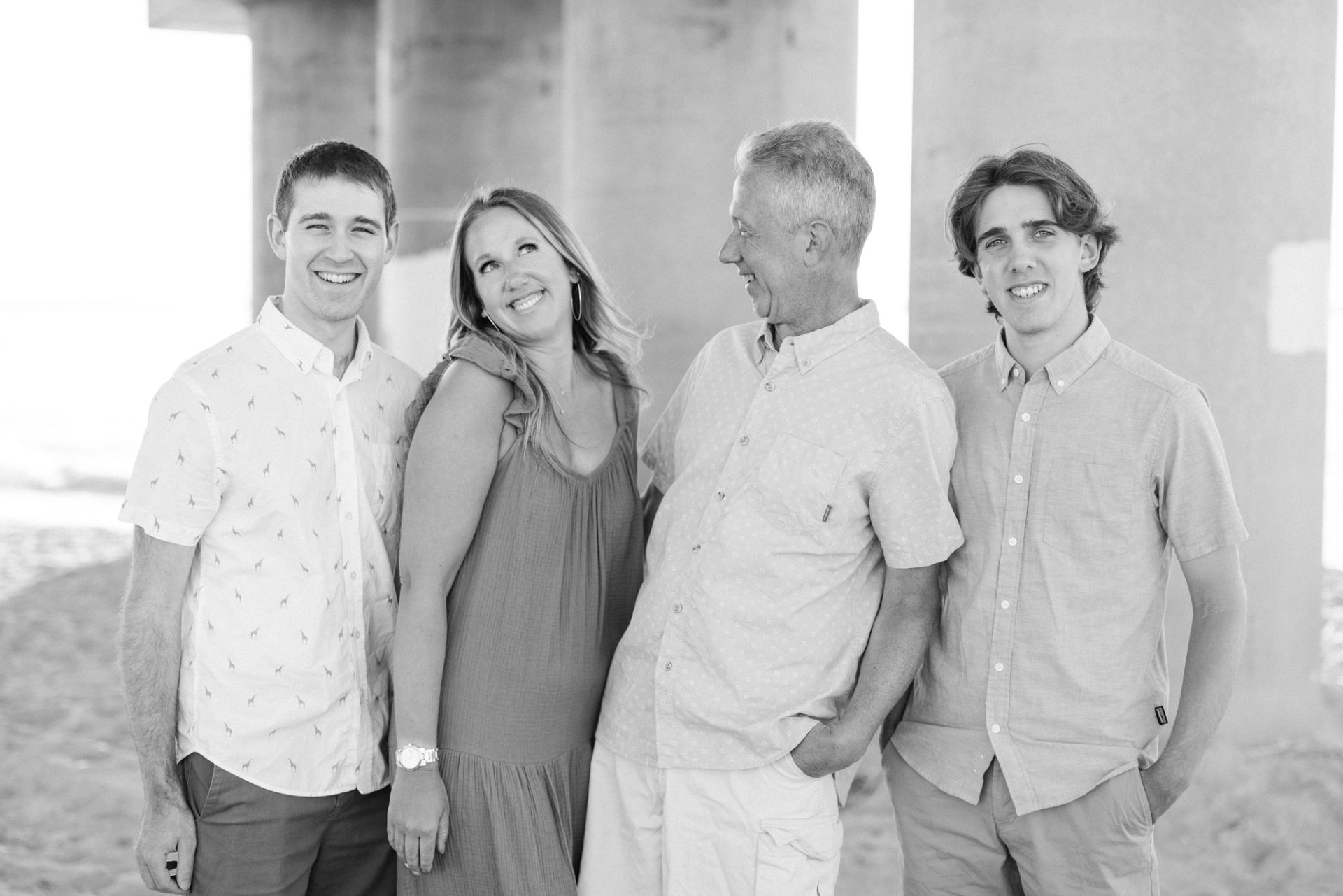 A black and white photograph of four family members leaning together against a concrete piling under the bridge in Ocean City, New Jersey