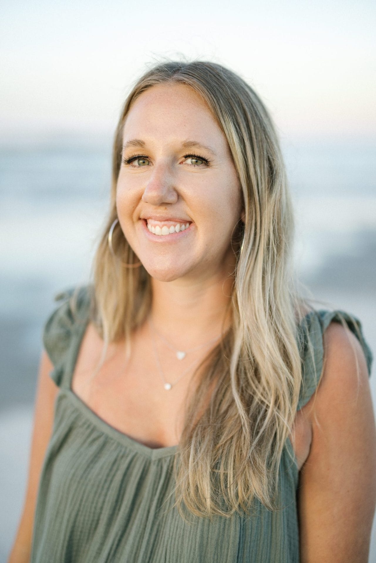 An individual portrait of a smiling woman in a long green dress with the surf soft behind her in Ocean City, New Jersey