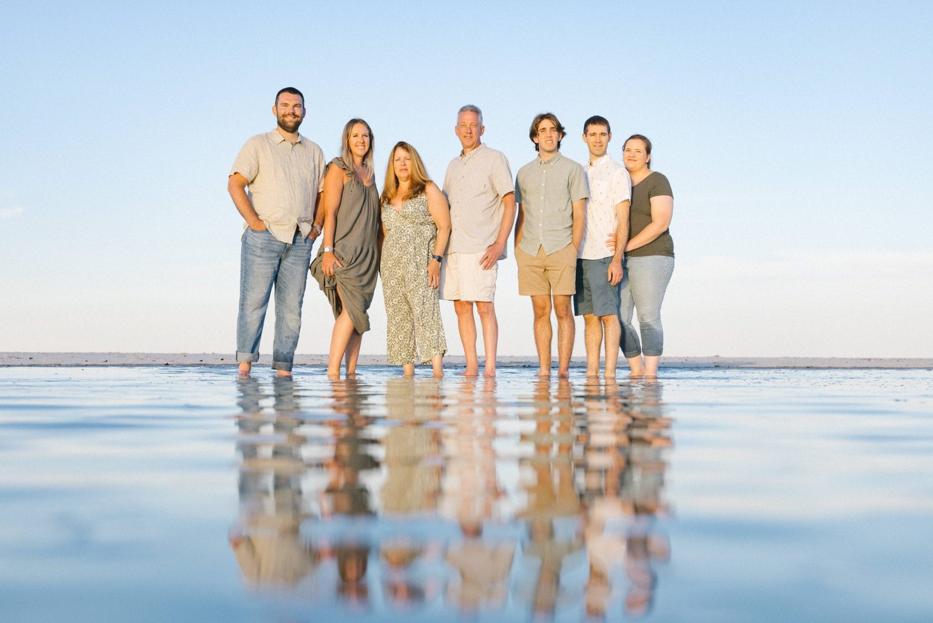 The whole family standing barefoot in a shallow film of water with a full mirrored reflection underneath them in Ocean City, New Jersey
