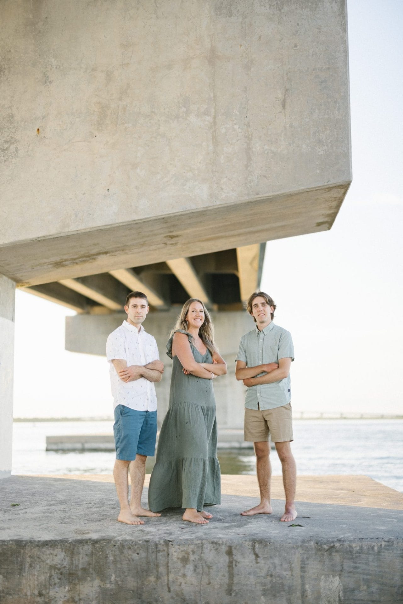 Three family members standing side by side with their arms crossed, the bridge running off behind them over the water in Ocean City, New Jersey