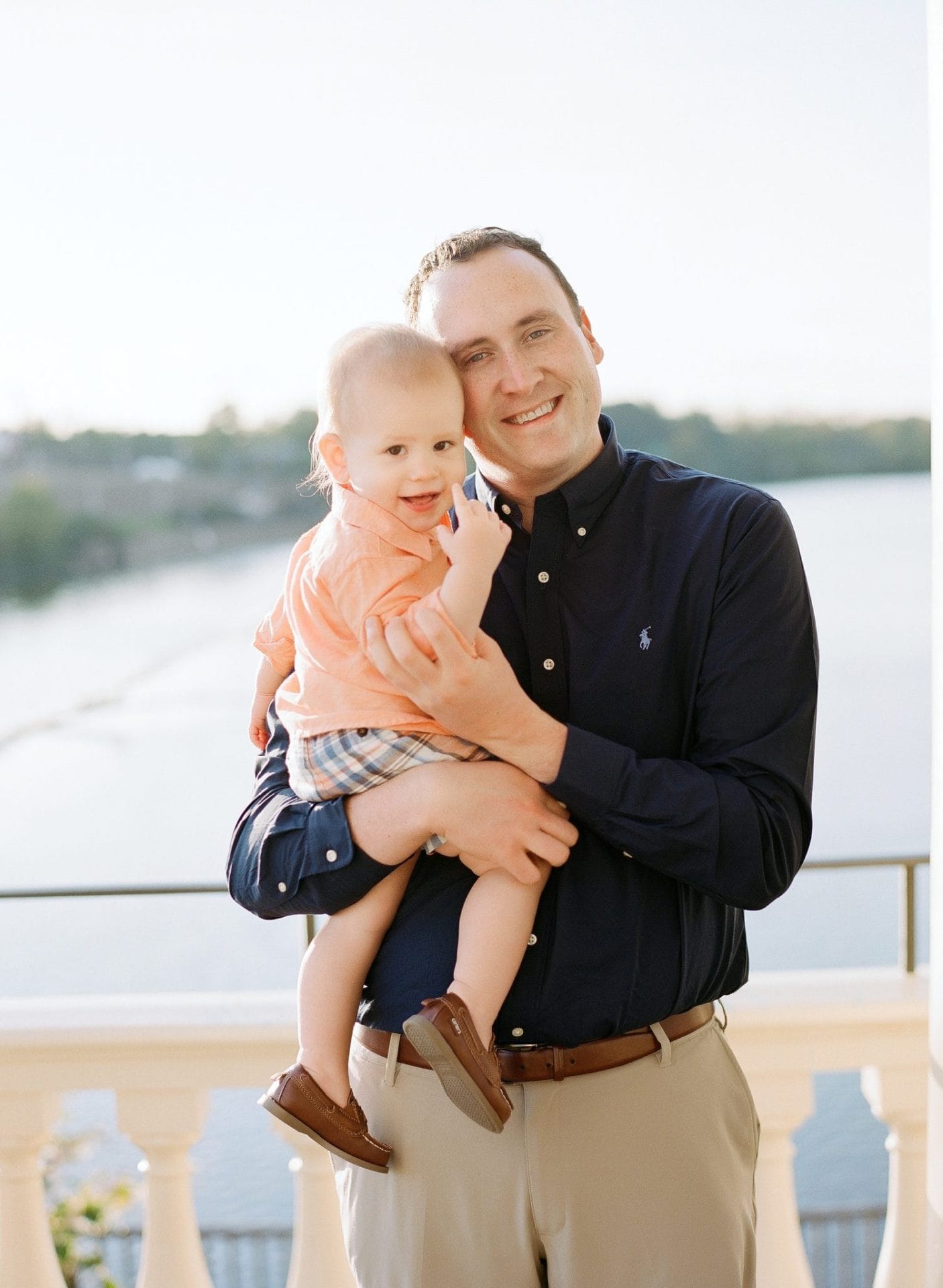 A dad holding his grinning son with the river and a railing behind them at the Philadelphia Water Works