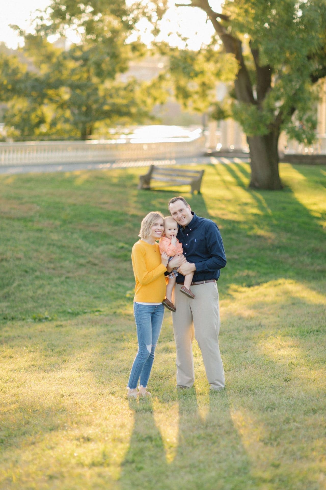 A family standing together on a sunlit lawn with long golden shadows and a large tree beside them at the Philadelphia Water Works