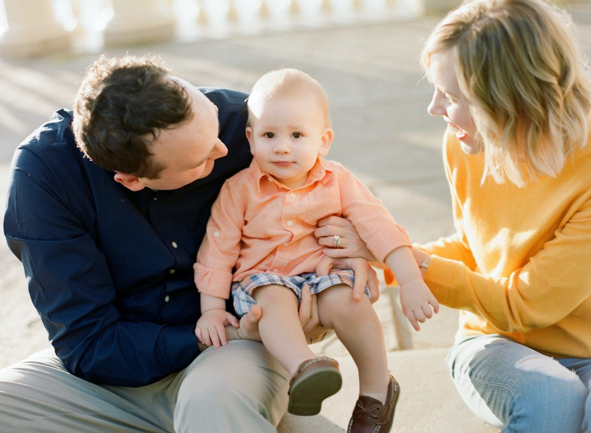 A mom and dad sitting on a stone step with their son on his dad's lap during a family session at the Philadelphia Water Works