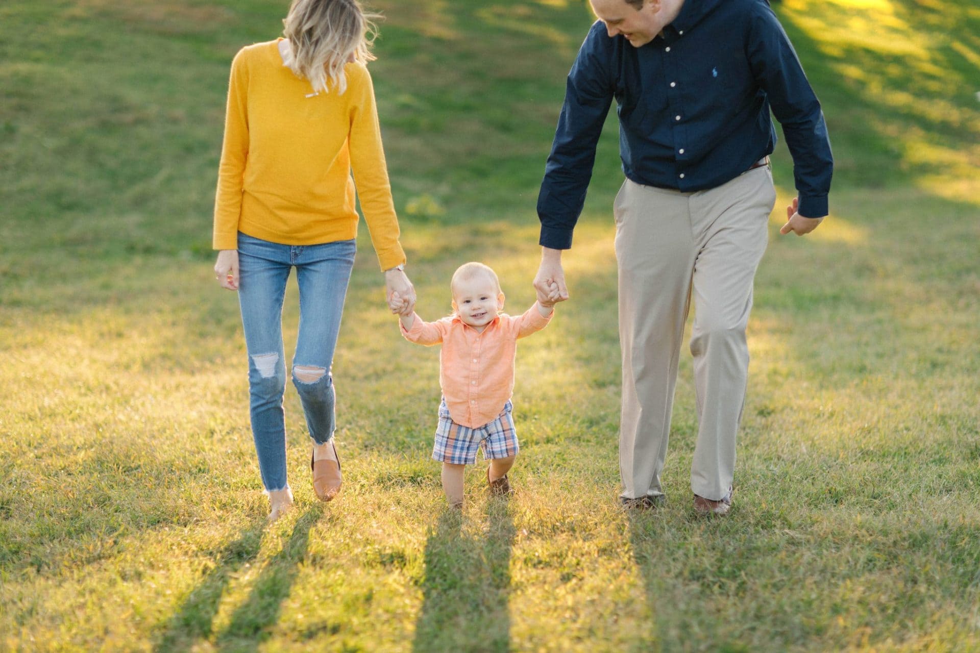 A mom and dad walking their son by both hands with the low sun behind them at the Fairmount Water Works in Philadelphia
