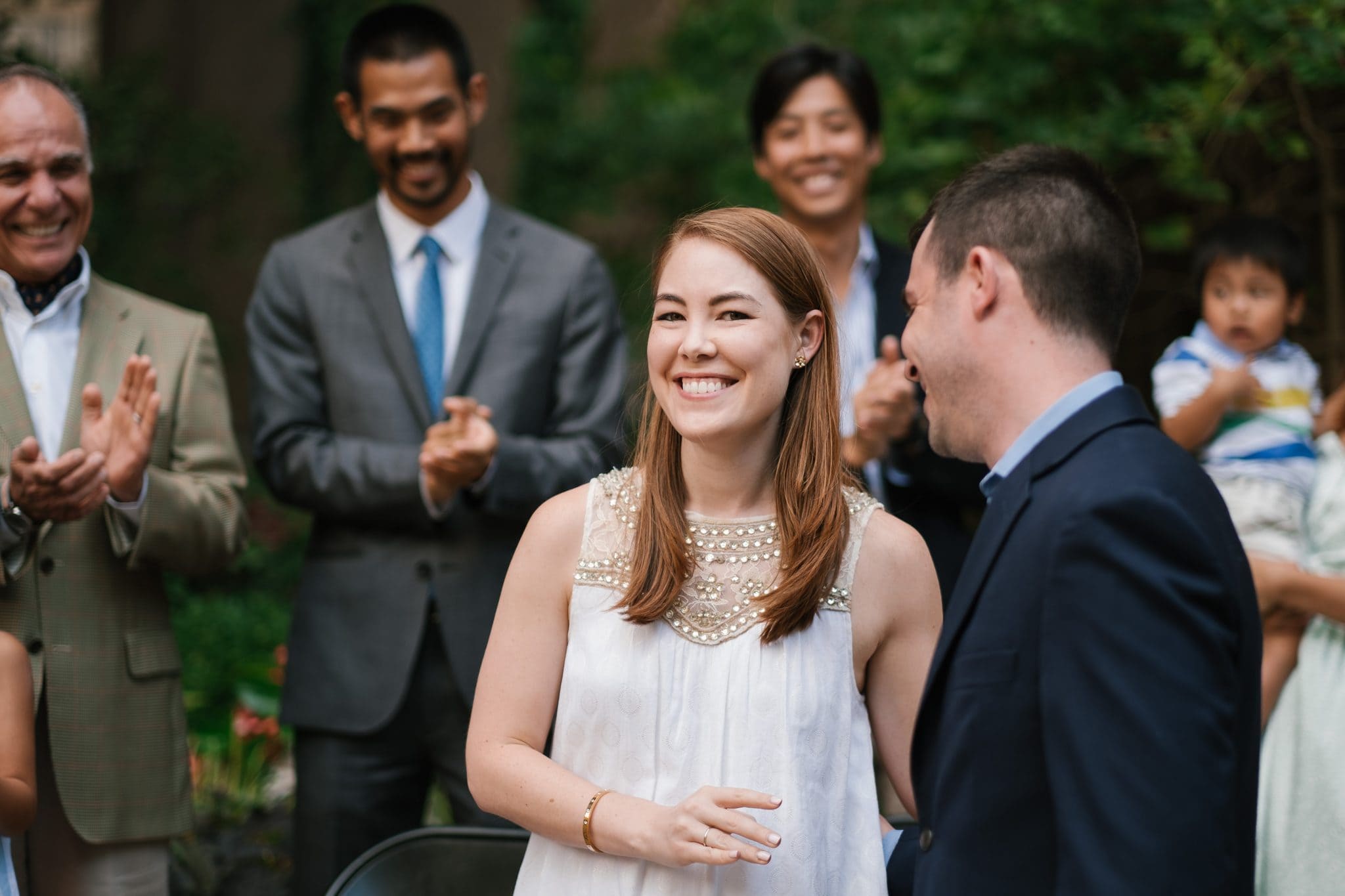 A newly engaged couple together as the family celebrates behind them at The Rittenhouse in Philadelphia